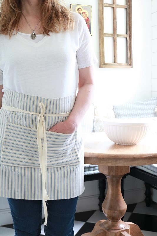 Farmhouse Style Pocket Apron - wearing in kitchen, at table, facing out with hand in pocket