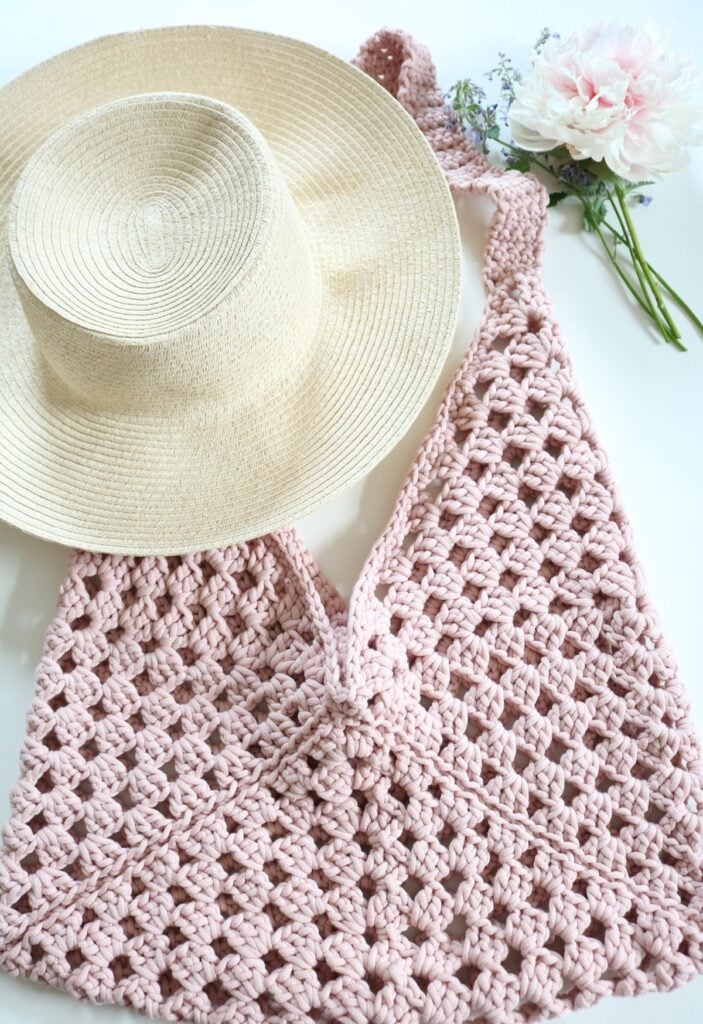 granny square crochet bag on table with hat and flowers